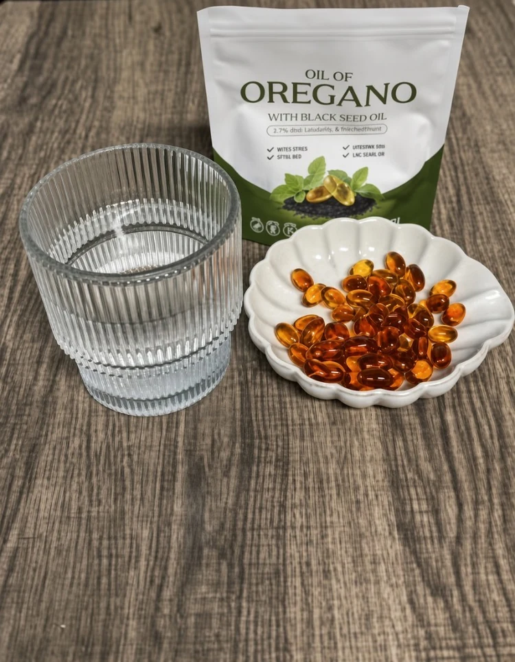 Oil of oregano pouch with black seed oil, a glass of water, and softgels in a dish